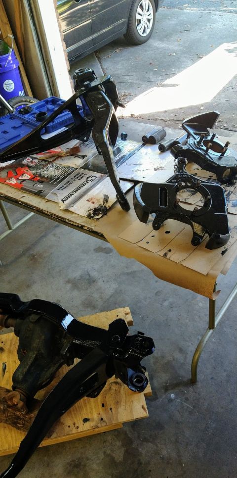 1996 Ford Bronco - Several black painted suspension components, including control arms and a spindle, are laid out on a table and on a wooden pallet. The scen…