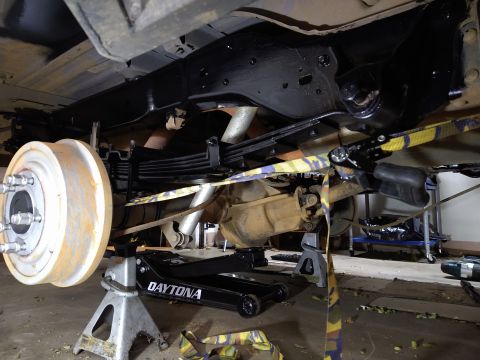 1996 Ford Bronco - The underside of a vehicle is shown, supported by jack stands. Visible components include the rear axle, leaf springs, brake drum, and a fr…