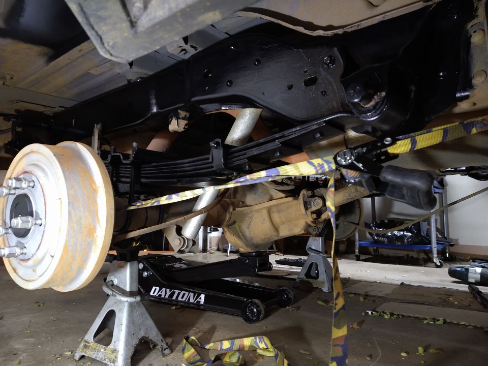 Underside of a vehicle on jack stands, showing rear axle, leaf springs, and brake drum.