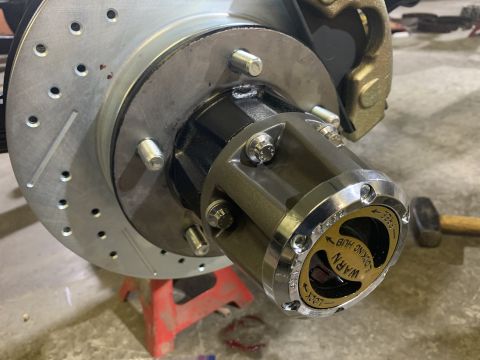 1979 Jeep CJ5 - A close-up view of a vehicle's front hub assembly, featuring a slotted and drilled brake rotor, a gold and black Warn locking hub with text…