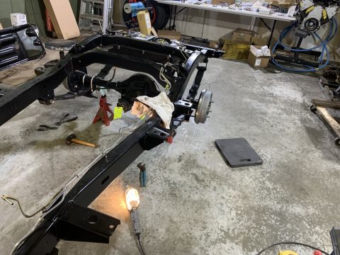 1979 Jeep CJ5 - A black Jeep CJ5 frame is elevated on jack stands in a garage setting. Various tools, including a sledgehammer and pliers, are scattered ar…