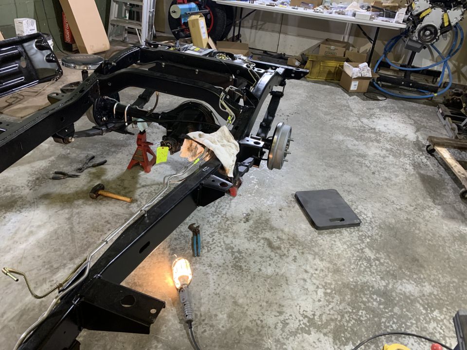 Black Jeep CJ5 frame on jack stands with tools in a garage.
