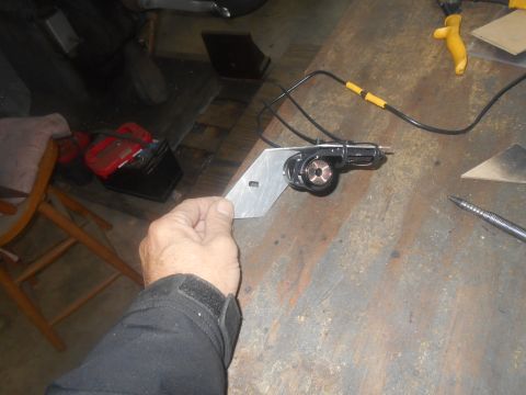 1992 Ford Bronco - A person's hand holds a metal bracket with a black device attached to it. The bracket is being held over a workbench.