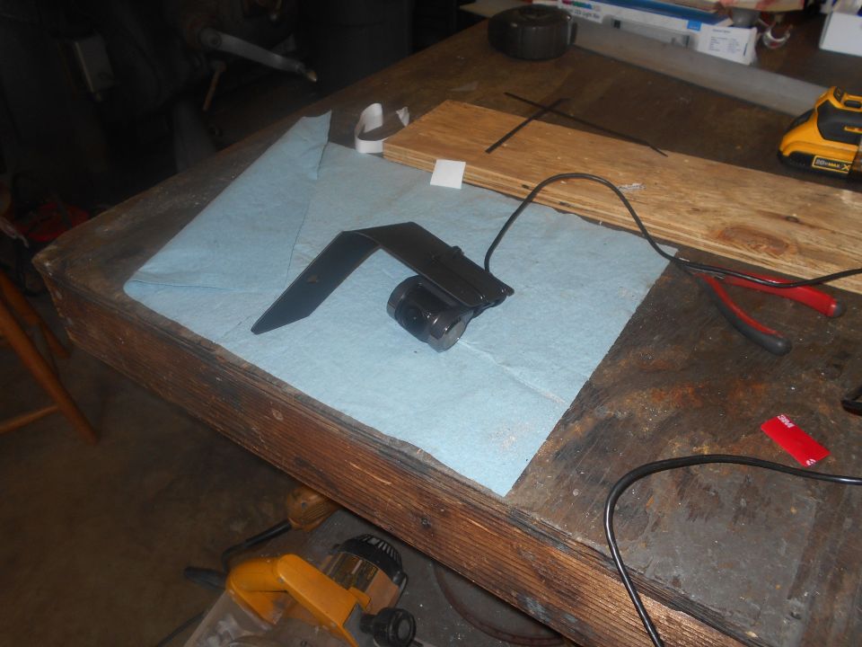 Black metal bracket with a cylindrical component on a blue paper towel on a workbench.