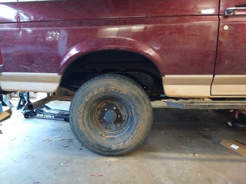 1996 Ford Bronco - The rear passenger side of a maroon Ford Bronco is shown, lifted on a jack and jack stands. The wheel is a Cooper Discoverer ATP tire on a…