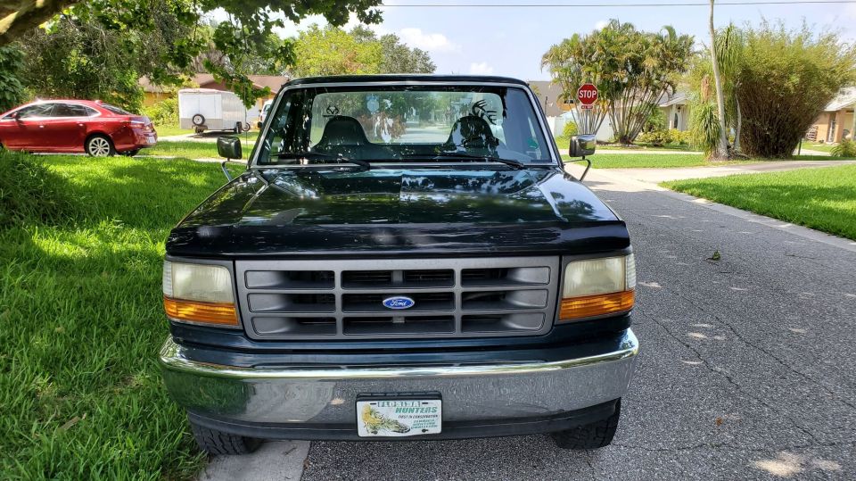 Front view of a dark green Ford pickup with chrome bumper and Florida plate on a residential street