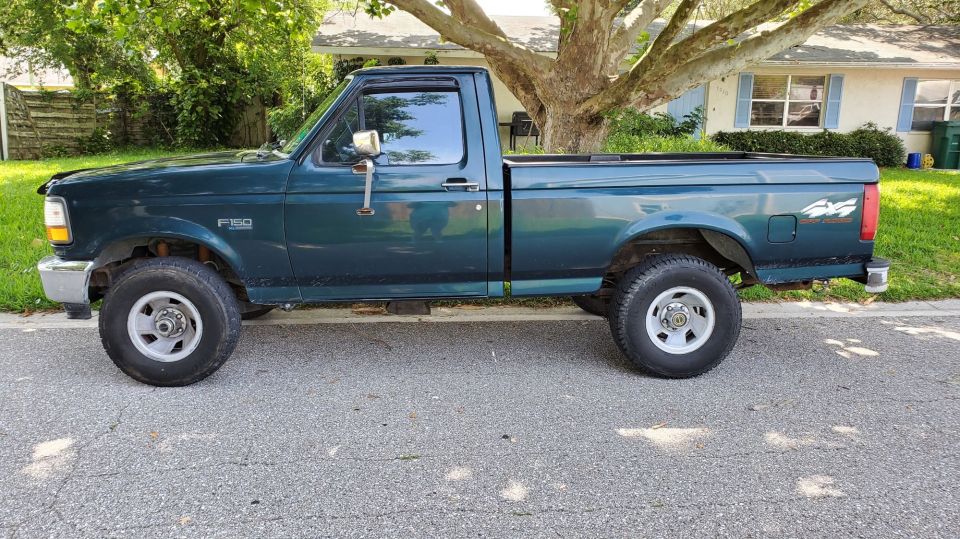 Dark green Ford F-150 regular cab pickup, driver-side view, parked on a residential street