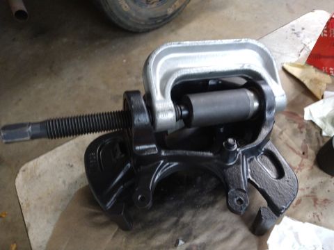 1996 Ford Bronco - A C-clamp is being used to press a bearing into a black metal automotive suspension component, likely a steering knuckle or spindle. The co…