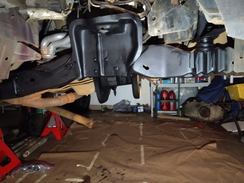 1996 Ford Bronco - Underneath view of a vehicle frame and exhaust system, with a transmission and other parts visible in the background. The vehicle appears t…