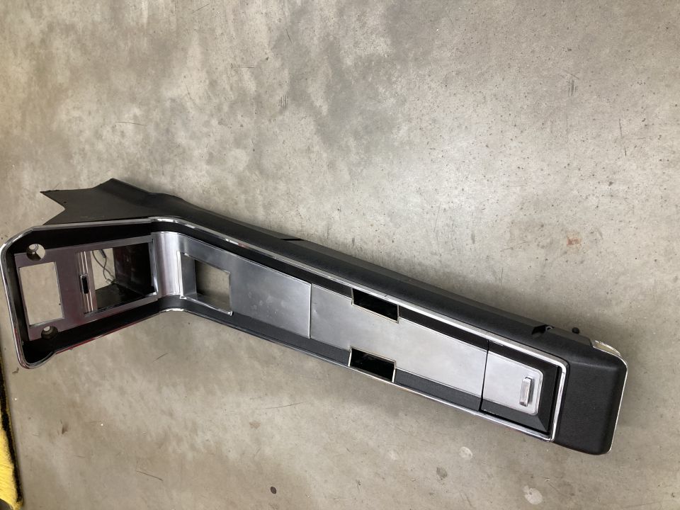 Black and chrome automotive center console trim piece with cutouts