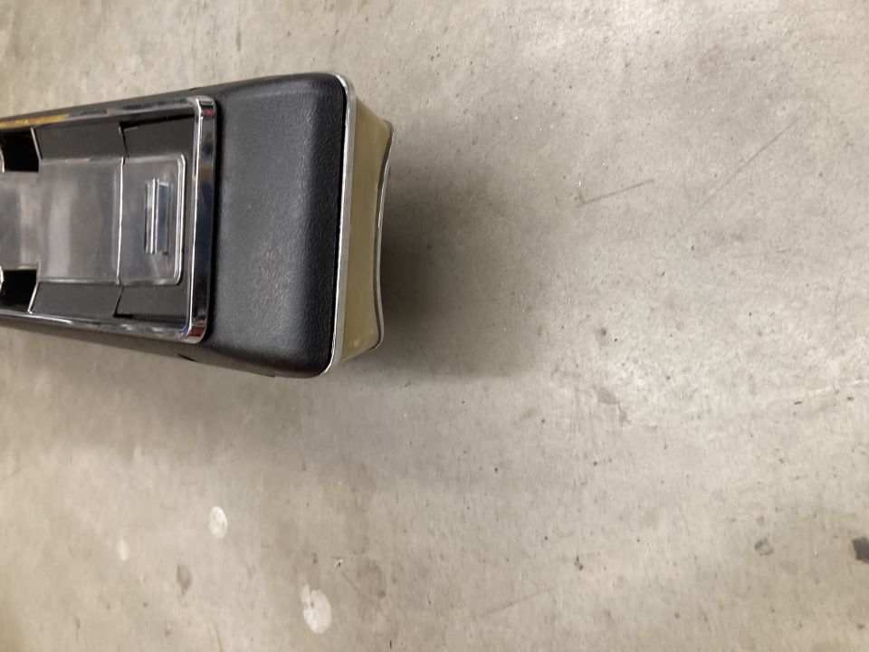 Black and chrome automotive center console part with beige trim on concrete.