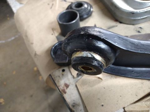 1996 Ford Bronco - A close-up view shows a black suspension control arm with a brass bushing and rubber boot. Other automotive parts and tools are visible in…