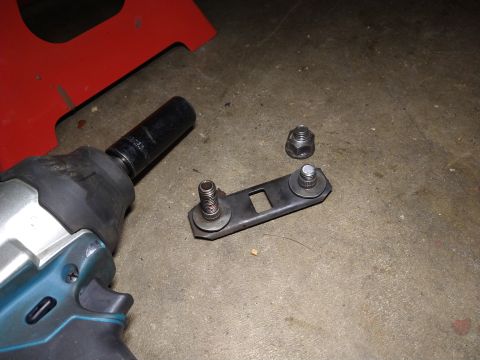 1996 Ford Bronco - A close-up shot shows a metal bracket with two bolts attached, along with a separate nut and an impact wrench socket on a concrete floor. A…