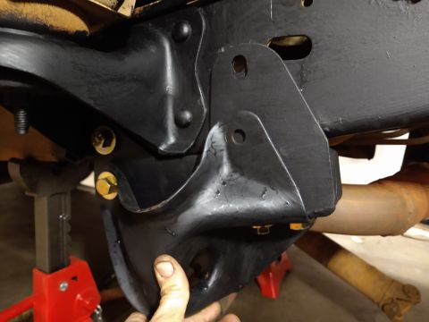 1996 Ford Bronco - A close-up view shows a black metal suspension component bolted to the frame of a vehicle, with a hand reaching in to hold it. The vehicle…