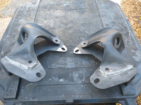 1996 Ford Bronco - Two black metal brackets with visible welds are placed on a dark gray textured surface. The brackets appear to be automotive parts, possibl…