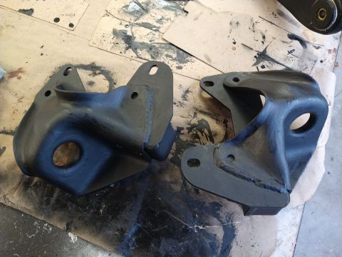 1996 Ford Bronco - Two suspension brackets painted black sit on a surface covered with paper and paint splatters.