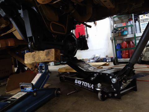 1996 Ford Bronco - The undercarriage of a vehicle is elevated on jacks and wooden blocks, indicating maintenance or modification work.