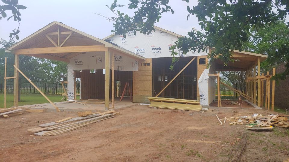 Garage and carport under construction with lumber and Tyvek wrap visible