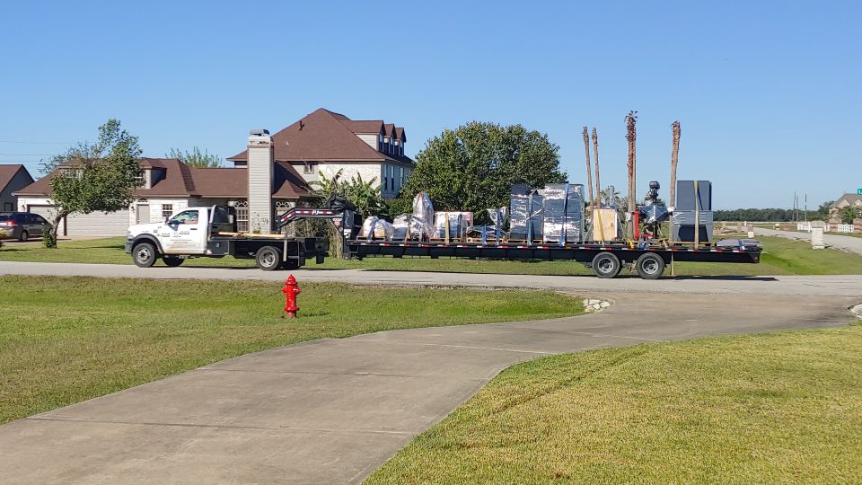 White flatbed truck towing a trailer loaded with various equipment and materials