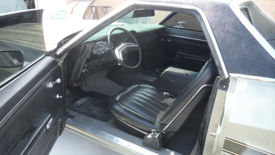 Interior of a vintage Ford Ranchero, driver's side door open, showing black seats and dashboard.
