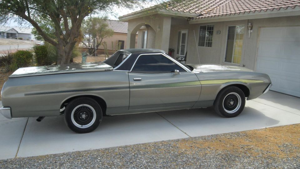 Silver 1972 Ford Ranchero with black vinyl top and side stripes parked in front of a house.