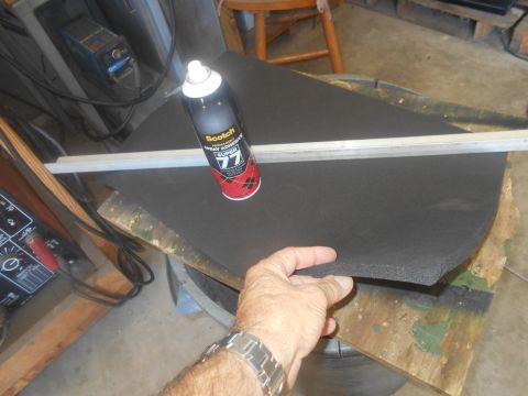 1992 Ford Bronco - A hand holds a piece of black foam material next to a can of spray adhesive and a metal ruler. The foam is resting on a wooden surface, and…