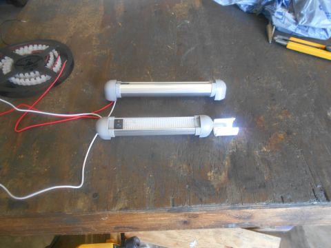 1992 Ford Bronco - Two LED light bars with switches are laid out on a wooden surface next to a roll of LED strip lights. One of the light bars is illuminated.