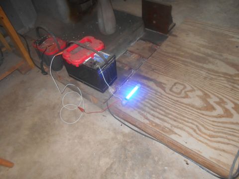 1992 Ford Bronco - Two car batteries are connected to a glowing blue light tube. The setup is on a wooden surface next to a concrete floor.