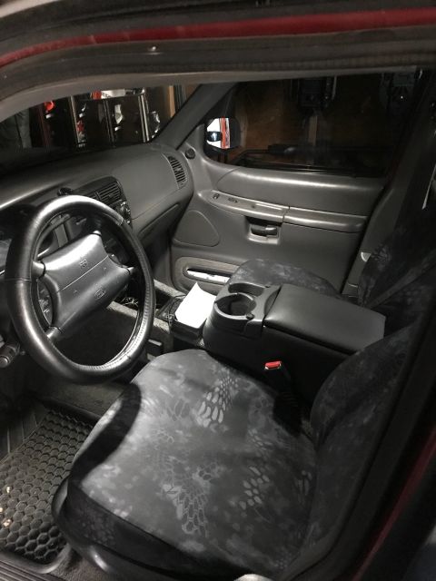 2000 Ford Explorer - The interior of a Ford Explorer shows a black steering wheel, gray dashboard, and front seats with custom camouflage seat covers. A center…
