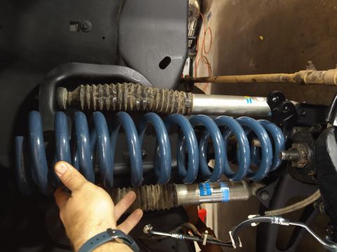 1996 Ford Bronco - A person's hand is holding a blue coil spring next to a silver Bilstein shock absorber and a ribbed rubber boot, likely part of a vehicle's…