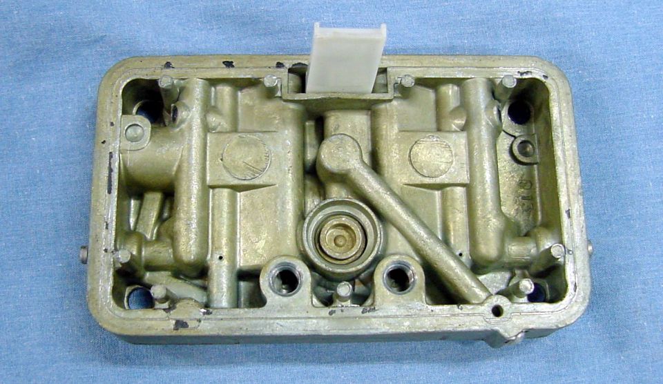 Internal view of a carburetor with brass-colored metal housing and white plastic component.