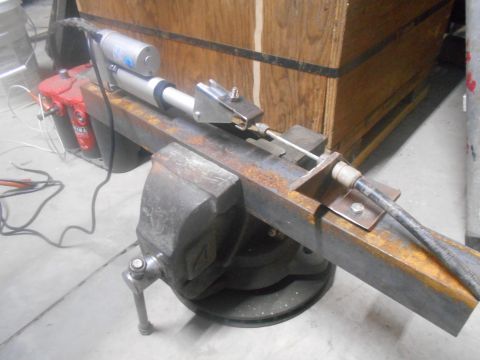 1992 Ford Bronco - A close-up view of a mechanical actuator assembly mounted in a vise. The assembly includes a red motor and a silver cylinder, connected to…