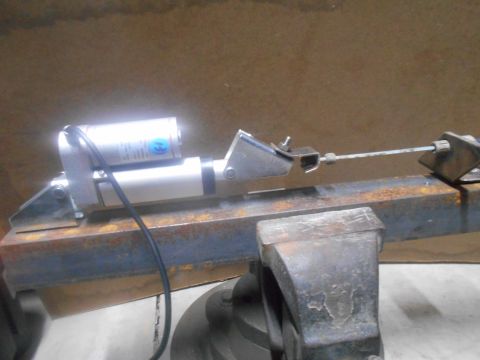 1992 Ford Bronco - A close-up view of a mechanical actuator attached to a rusty metal beam, which is held in a vise. The actuator has a silver cylinder with a…
