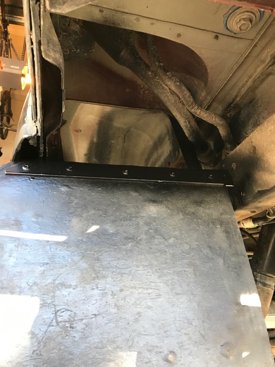 Underside view of a vehicle showing a black metal plate attached to the frame.