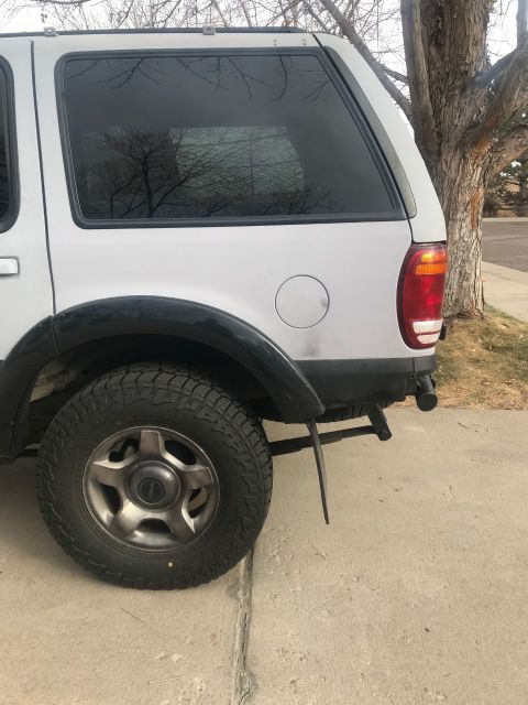 2000 Ford Explorer - The rear passenger side of a silver SUV is shown parked on a concrete driveway next to a tree. Visible details include a black fender flare…