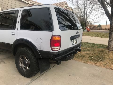 2000 Ford Explorer - The rear passenger side of a white 2000 Ford Explorer is shown parked on a concrete driveway. It features a black aftermarket bumper with a…