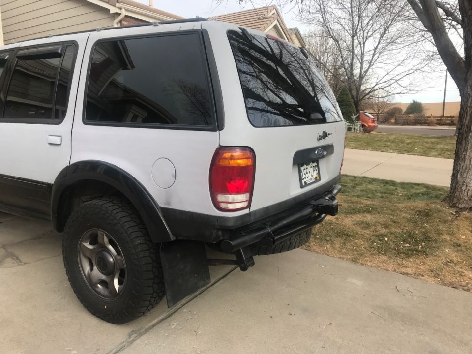 White 2000 Ford Explorer rear passenger side with aftermarket bumper and tow hitch.