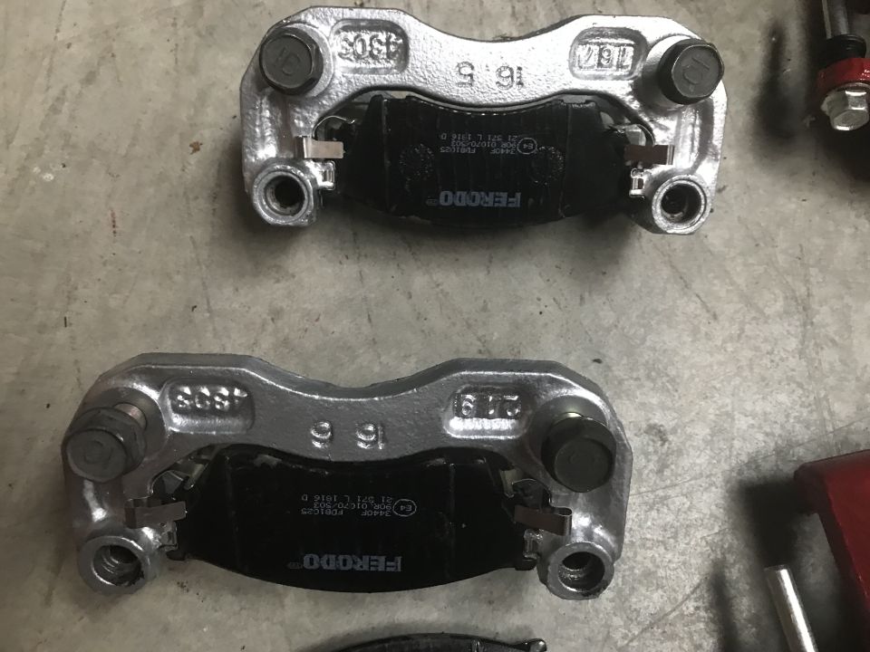 Two silver brake calipers with black Ferodo brake pads on a concrete surface.