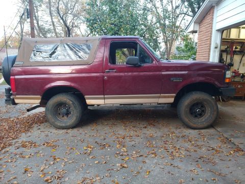1996 Ford Bronco - Side view of a maroon 1996 Ford Bronco a tan soft top and two-tone paint.