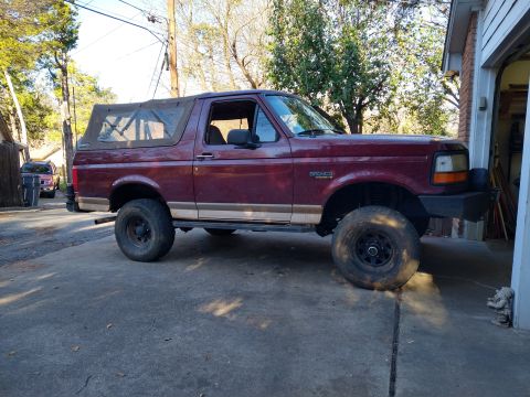 1996 Ford Bronco - Maroon 1996 Ford Bronco with a soft top and lifted suspension parked in a driveway.