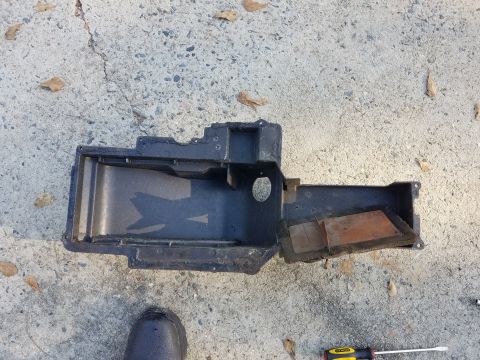 1976 Ford Ranchero - A black plastic heaterbox part, likely for a vehicle, rests on a concrete surface with fallen leaves.