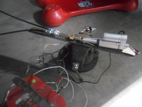 1992 Ford Bronco - A mechanical part is secured in a vise, connected to wires and a battery, with a red object in the background.