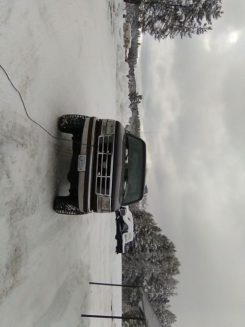 1995 Ford Bronco - A dark brown Ford Bronco is parked in a snowy area, with another white vehicle visible behind it.