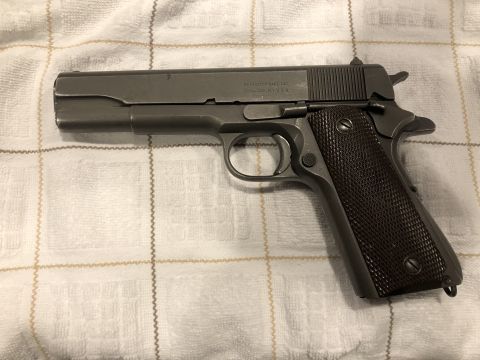 1995 Mercury Grand Marquis - Left-side view of a parkerized M1911A1-pattern pistol with brown checkered plastic grips, laid on a white grid-patterned blanket. The slide…
