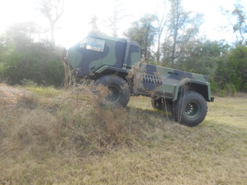 1992 Ford Bronco - This military truck is shown on a grassy incline with trees in the background.
