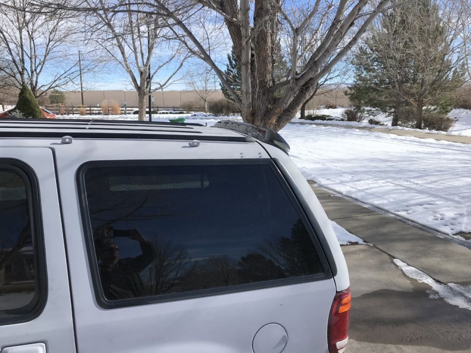 Silver SUV rear quarter panel with tinted windows and roof rack. Snow on the ground