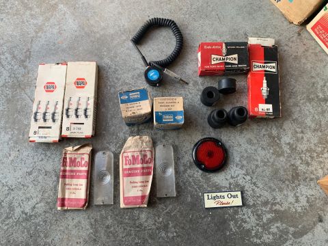 1993 Ford Bronco - Assorted vintage automotive parts including spark plugs, grommets, and a timing light are laid out on a concrete surface.