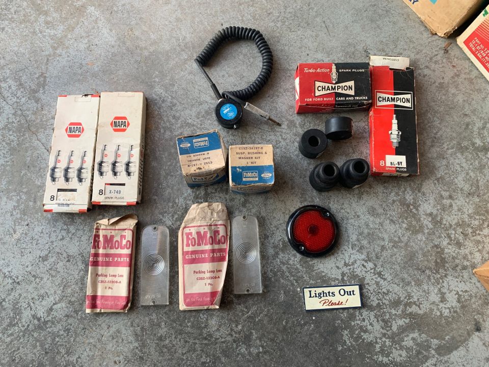 Collection of NAPA and FoMoCo spark plugs, rubber grommets, a taillight lens, and a timing light