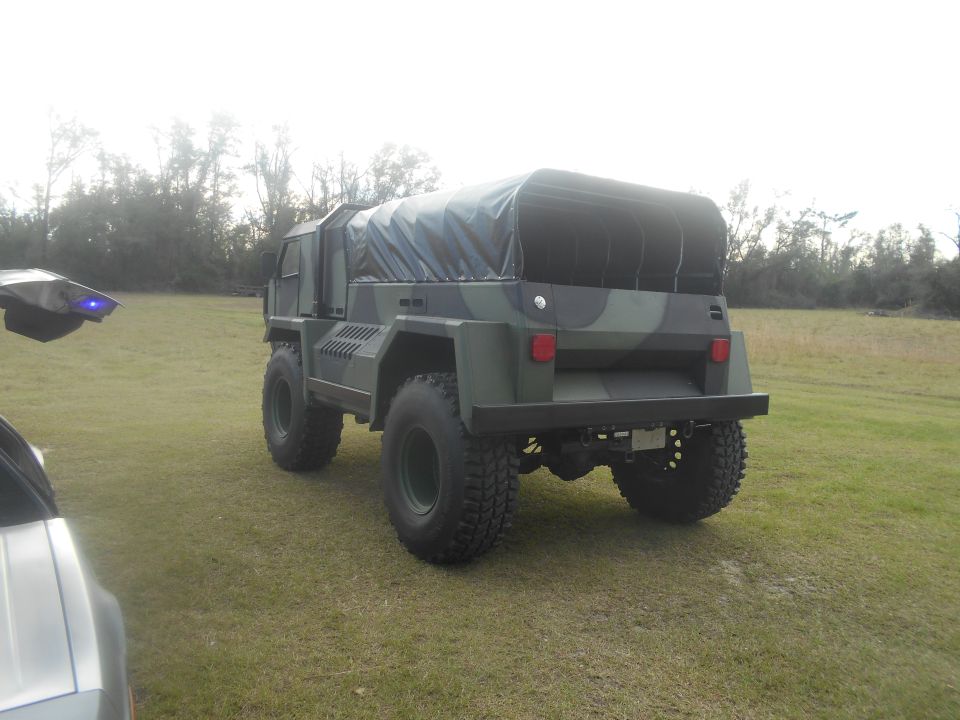 Camouflaged military-style truck with black canvas top, rear view.