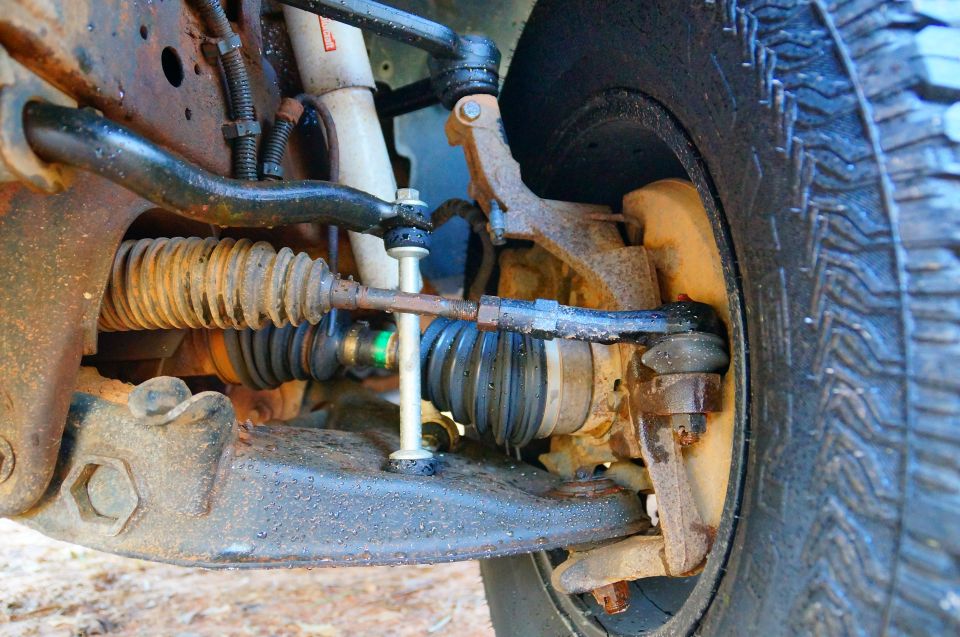 Close-up of wet and rusty truck suspension parts including tie rod ends and sway bar links.